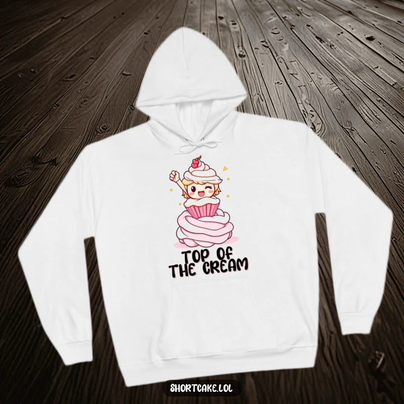 Funny shortcake character in a triumphant pose on a whipped cream swirl, depicted on a cozy hoodie for ultimate comfort.